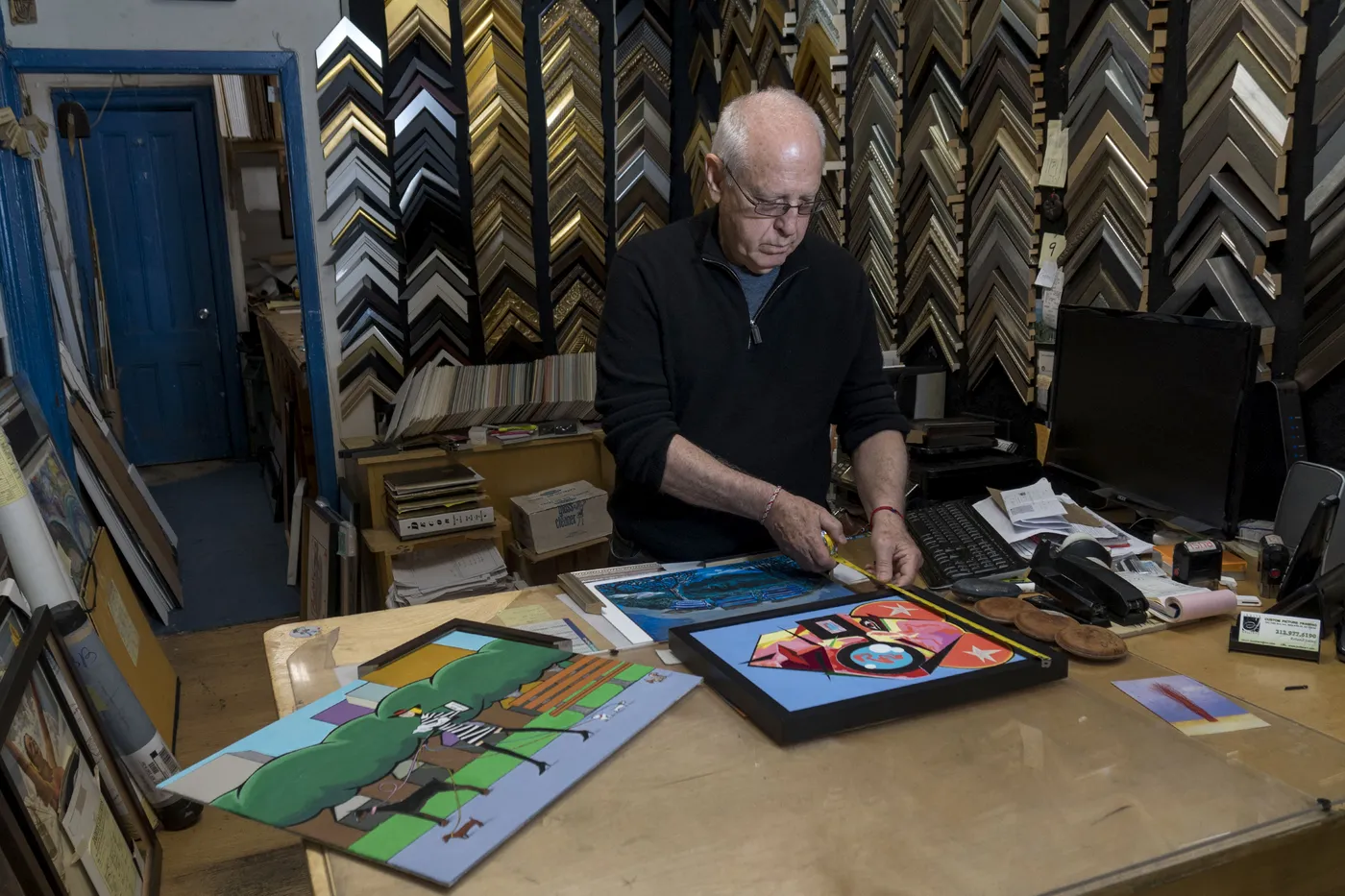 Framer measuring artwork to size against the wall of moulding samples